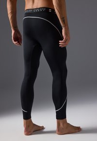 Black athletic leggings with reflective silver accents and a wide waistband featuring brand logo. Made of stretchy, smooth material.