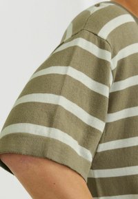 Olivenfarvet stribet T-shirt med hvide vandrette striber. Blød tekstur og korte ærmer. Udsigten fokuserer på ærmedetaljer og pasform.