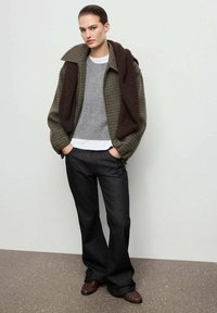 Chaqueta de cuadros marrón de gran tamaño, suéter gris, camisa blanca, pantalones anchos oscuros y mocasines marrones; texturas suaves y un look en capas.