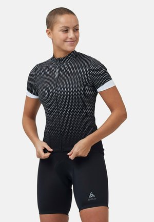 Kurzärmliges Radsporttrikot in Schwarz mit weißen Punkten, ausgestattet mit einem Reißverschluss vorne und weißen Bündchen, kombiniert mit schwarzen Radsportshorts.