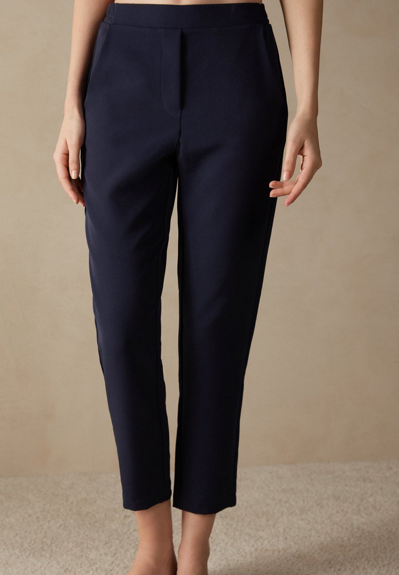 Pantaloni tailor navy blu con una texture morbida, vita medio-alta e taglio alla caviglia, caratterizzati da piega frontale e tasche laterali.