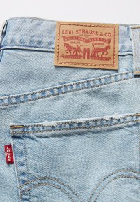 Light blue denim jeans feature a brown leather patch labeled "Levi Strauss & Co." with red logo and stitching details. Red tab on pocket.