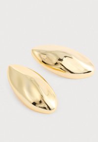 To shiny guld forlængede ovale metalobjekter med glatte, buede overflader på en ensfarvet hvid baggrund.