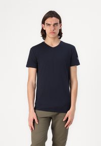 T-shirt blu navy a V in morbido cotone, con maniche corte e design aderente. Logo minimalista sulla manica sinistra.