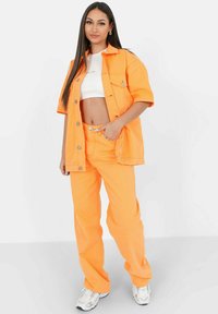 Chaqueta de mezclilla naranja brillante y pantalones a juego, combinados con un top corto blanco. Presenta un cierre de botones y un ajuste relajado.
