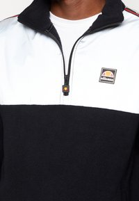 Fleece halvdraget pullover i svart och vitt med logomärke, med ribbad krage och kontrasterande tygtextur. Dragkedja vid halsen.