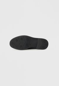 Semelle de chaussure en caoutchouc noir avec surface texturée, poignées circulaires et section intermédiaire lisse. Conçue pour l'adhérence et la durabilité.