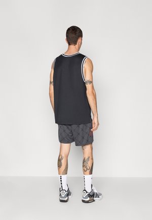 Un débardeur noir avec des bords blancs, associé à un short gris à motifs. Des chaussettes blanches avec des accents noirs et des baskets noires.
