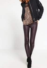 Černá bomber bunda přes top s leopardím vzorem, doplněná lesklými burgundskými legínami a černými kotníkovými botami. Hladké textury a přiléhavý střih.