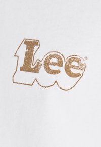 Biała bawełniana tkanina z dużym, teksturowanym złotym logo "Lee", o lekko postarzonym wykończeniu i zaokrąglonych literach.