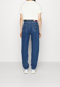 Světle šedé tričko, modré džíny s vysokým pasem a uvolněným střihem, s zadními kapsami a štítkem, doplněné o bílé tenisky.