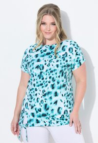 Kortärmad topp med turkos och svart djurmönster, med en knutdetalj på sidan och en avslappnad passform. Mjuk tygtextur.