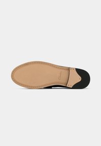 Sola de couro de um sapato de vestido preto com costura detalhada e um logótipo da Clarks próximo ao arco, apresentado contra um fundo branco.