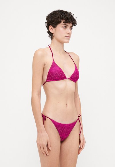 Magenta bikini with a triangular top and adjustable ties. Textured fabric features zigzag patterns. Designed for a minimal coverage fit.