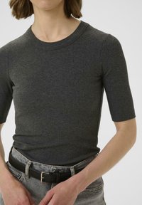 Tumehall ribiga lühikeste varrukatega topp, millel on ümar kaelus, kombineeritud kõrge vöökohtadega heledate teksadega ja musta vööga.