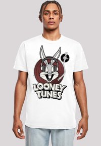 Balta kokvilnas T-kreklu ar grafiku, kurā attēlots karikatūru zaķis ar austiņām, apņemts ar sarkanu apļa dizainu un tekstu "Looney Tunes".