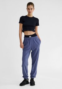 Zwarte cropped ribbed t-shirt gecombineerd met losse lavendelkleurige sweatpants met een elastische tailleband en zijzakken. Zwarte sneakers.