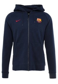 Felpa con zip navy in tessuto testurizzato, dotata di un logo frontale del FC Barcelona e dello swoosh rosso di Nike. Include due tasche anteriori e cappuccio con cordino.