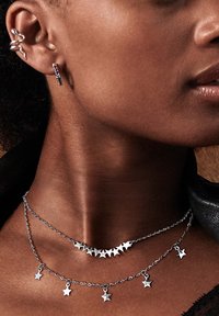 Bijoux en argent comprenant des colliers superposés avec des pendentifs en forme d'étoile et un design à pointes. Boucles d'oreilles de style crochet également en argent.