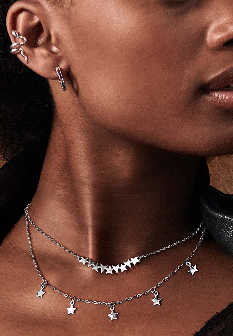 Bijoux en argent comprenant des colliers superposés avec des pendentifs en forme d'étoile et un design à pointes. Boucles d'oreilles de style crochet également en argent.
