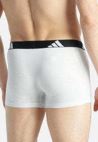 Vita boxertrosor med en svart elastisk midjeband som har Adidas-logotypen, slät textur och en åtsittande design. Bakvy visas.