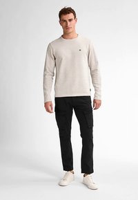 Vaalea beige teksturoitu pitkähiha-paita, jossa vaakasuorat raidat, yhdistetty mustiin cargo-housuihin useilla taskuilla ja valkoisiin lenkkareihin.