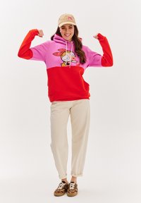Hnědo-červený a růžový barevně blokovaný hoodie s grafikou kreslené postavičky, kapuce se šňůrkou, v kombinaci s béžovými kalhotami a teniskami s leopardím potiskem.