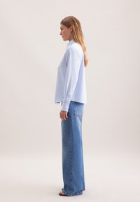 Blusa a righe blu chiaro e bianca con maniche lunghe, abbinata a jeans in denim blu chiaro a vita alta, con una vestibilità comoda e dettagli minimi.