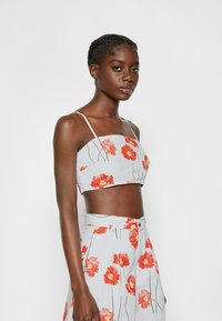 Top cropped cinza com estampa de papoilas vermelhas, apresentando alças finas e um decote quadrado, acentuado por caules verdes.