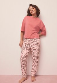 Světle růžové krátké bavlněné tričko s krátkými rukávy spojené s bílými pyžamovými kalhotami s potiskem srdcí v odstínech červené a růžové.