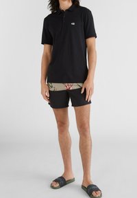 Polo noir, short de bain noir court avec ceinture florale, claquettes grises et vertes, coupe décontractée, matériau en coton.