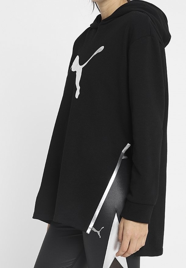 Personne portant un sweat à capuche Puma noir avec logo argenté et des leggings noirs assortis avec logo Puma argenté et motif sur le côté.
