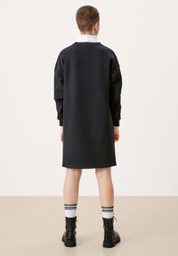 Vestido sudadera negro de gran tamaño con mangas largas, un cuello blanco y puños acanalados, combinado con botas de combate negras y calcetas a rayas.