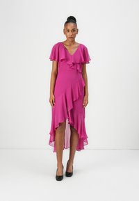 Robe fuchsia avec des manches à volants et un ourlet asymétrique. Fabriquée en tissu léger, elle présente un col en V et un design en couches.