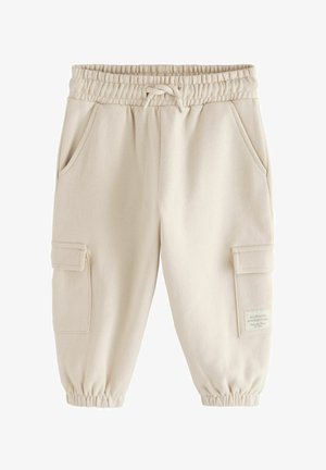 Beige cargobukser i sweatshirtstof med elastisk linning og manchetter, forlommer samt lommer med lapper på lårene og et lille trykt mærke på højre side.