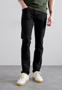 Fekete, slim fit farmernadrág, pamut keverékből készült, fehér sportcipőkkel párosítva. Az öltözet laza stílusú, alkalmas mindennapi viseletre.