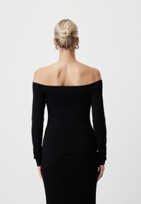 Crni top s otvorenim ramenima, prilagođenog kroja, dugih rukava i rebraste teksture. Glatka tkanina prelazi u odgovarajuću crnu suknju, ističući elegantnu siluetu.