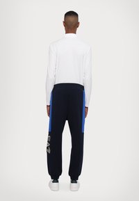 Vit långärmad pikétröja i kombination med marinblå joggers med blå sidopaneler och logodetalj. Bekväm passform med smalnande anklar.