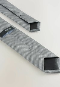 Schwarz-weißer gemusterter Krawatte aus strukturiertem Stoff. Sie verfügt über ein schlankes, rechteckiges Design und ein gefaltetes Ende. Markenlabel ist sichtbar.