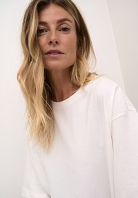 T-shirt bianca oversize realizzata in morbido cotone, con un piccolo logo ricamato sul petto e maniche corte morbide.