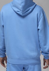 Sweat à capuche bleu clair avec cordon de serrage, poignets et ourlet côtelés. Fabriqué en tissu doux à la texture lisse, avec des détails minimaux dans le dos.