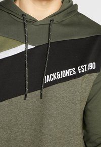 Felpa verde oliva con blocchi di colore neri e grigi, con il logo bianco "JACK&JONES EST.1990", cappuccio con coulisse e texture morbida.