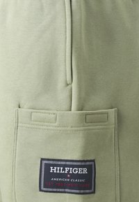 Pantalons de survêtement vert clair avec une poche arrière et une étiquette de marque cousue. Texture douce et détail de taille élastique visibles.