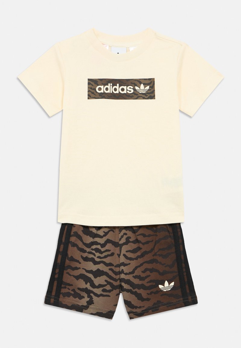 Camiseta Adidas de manga corta en color crema con logo de rayas de tigre en marrón y negro, combinada con pantalones cortos a juego con rayas de tigre y franjas negras.