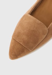 Zapato plano de ante marrón con punta puntiaguda y una amplia correa sobre la parte superior, con textura suave y diseño minimalista.