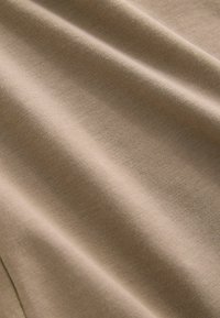 Beige bomuldsstof med en glat overflade, der udviser let str�æk og en subtil glans, med bløde folder og undulationer.