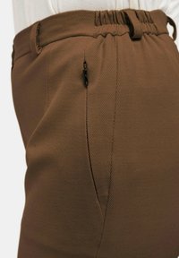 Brown, textured trousers featuring an elastic waistband, side pocket with zipper, and straight fit with subtle stitching details.