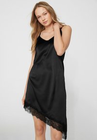 Vestido tipo slip de satén negro con una textura suave, con un dobladillo de encaje en la parte inferior y tirantes delgados para los hombros, diseñado con un corte asimétrico.