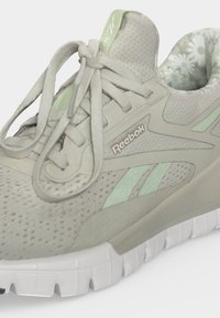 Ανοιχτό γκρι παπούτσι Reebok με λεπτομέρειες σε μέντα, λευκή σόλα και λουλουδάτο σχέδιο στην εσωτερική πλευρά του κολάρου της φτέρνας, δεμένο με κορδόνια.