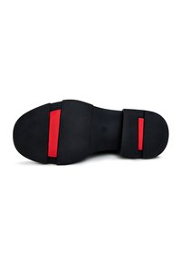 Suela de zapato negra con una superficie texturizada, un acento central rojo y un diseño segmentado distintivo para mejorar la tracción y la flexibilidad.